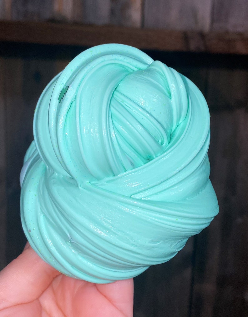 May include: A close-up of a light blue slime, with a smooth, glossy texture. The slime is folded and twisted into a ball shape.