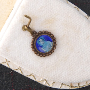 May include: A white velvet jewelry box with gold trim and the text "R. Dumoulin Bijoutier Bourges" inside. A small blue and gold pendant with a religious image is inside the box.