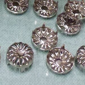Könnte beinhalten: Silberne Metallverzierungen mit Blumenmuster. Die Verzierungen haben eine erhabene Mitte und eine flache Rückseite.