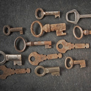 Puede incluir: Una colección de 11 llaves antiguas, algunas con diseños ornamentados, sobre una superficie gris oscuro. Las llaves son de metal y tienen una pátina oxidada.