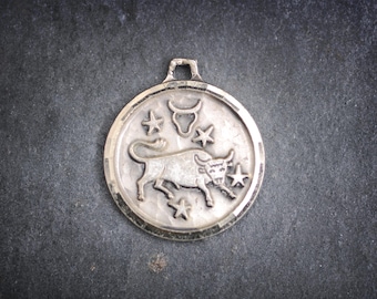 May include: Silver pendant featuring a bull zodiac symbol and stars. The pendant is round and has a silver chain.
