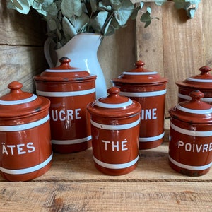 May include: Six vintage red enamel canisters with white lids and white lettering. The canisters are labelled "Pâtes", "Sucre", "Thé", "Vinaigre", "Poivre", and "Thé".