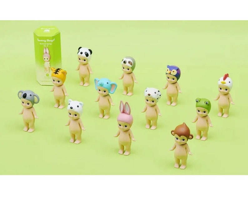 May include: A set of 12 small, nude-colored figurines wearing various animal hats. The hats include a panda, sloth, owl, chicken, koala, polar bear, bunny, frog, monkey, dalmatian, tiger, and elephant. The figurines are all standing on a green surface.