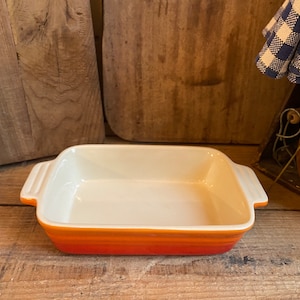 Puede incluir: Un pequeño plato para hornear rectangular con un interior blanco y rayas naranjas, amarillas y blancas alrededor del borde. El plato es de cerámica y tiene dos asas.