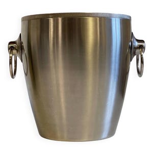 May include: A stainless steel wine bucket with a polished finish. The bucket has a flared shape, a textured rim, and two ring handles on either side. This beverage chiller is designed to hold a standard wine bottle.