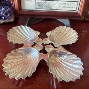 Puede incluir: Cuatro platos de plata en forma de concha, dispuestos en forma de cruz. Cada plato tiene un diseño texturizado en relieve que se asemeja a una concha.