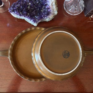 May include: Two round brown ceramic skillets with long handles and fluted edges. One skillet is positioned face up, while the other is placed face down on top, revealing a circular stamp on the base that reads Ceracron and West Germany.