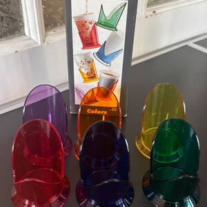 Peut inclure: Ensemble de porte-gobelets Guzzini colorés en rouge, violet, orange, bleu, vert et jaune. Les supports sont en plastique translucide et sont présentés avec leur boîte d'origine. La boîte affiche le logo Guzzini et le mot "Colors".