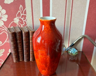 May include: A red ceramic vase with a glossy finish. The vase has a rounded body and a narrow neck.