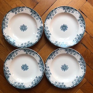 May include: Four white ceramic plates with a blue and green floral design. The plates have a raised rim and a center design.