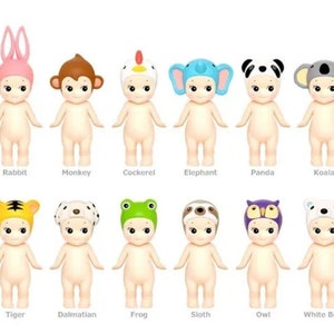 May include: A set of 12 adorable baby dolls wearing animal hats. The dolls are all nude-colored and have large, round eyes. The hats are a variety of colors and feature animals such as a rabbit, monkey, cockerel, elephant, panda, koala, tiger, dalmatian, frog, sloth, owl, and white bear.