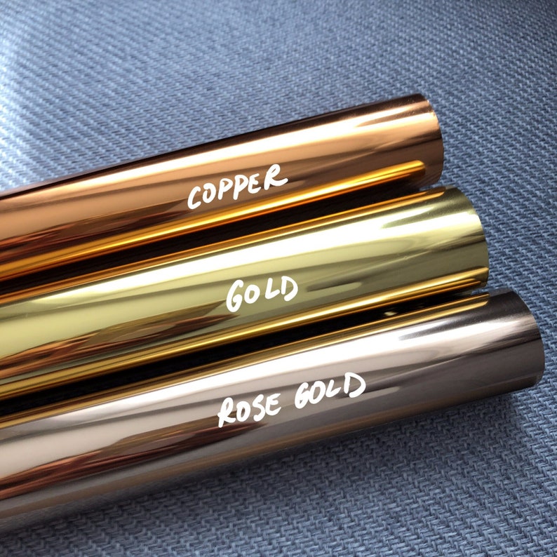 K&ouml;nnte beinhalten: Drei zylindrische Rollen aus Metallic-Folie, die horizontal angeordnet sind. Die oberste Rolle ist kupferfarben, die mittlere goldfarben und die untere ros&eacute;goldfarben. Jede Rolle tr&auml;gt eine wei&szlig;e handschriftliche Beschriftung: COPPER, GOLD, ROSE GOLD.