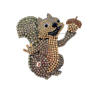 May include: A sparkly, multi-colored rhinestone squirrel brooch holding a rhinestone acorn. The squirrel is brown, orange, and green with black eyes.