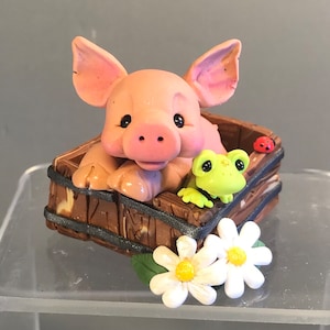 以下が含まれることがあります： 木製の浴槽に入ったピンクの子豚、緑のカエル、赤いテントウムシをあしらった気まぐれな置物。 黄色の中心を持つ2つの白いデイジーがベースにあります。 魅力的な装飾品です。