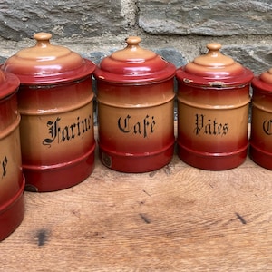 Peut inclure: Ensemble de six boîtes en émail vintage avec peinture rouge et beige. Les boîtes sont étiquetées avec les mots "Sucre", "Farine", "Cafi", "Pates", "Chicoree" et "Poivre".