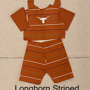 May include: A two-piece outfit for a doll, featuring a sleeveless top with a white Longhorn logo and striped shorts. The top and shorts are brown with white and green stripes.