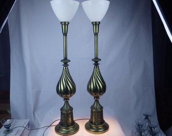 May include: A pair of tall, gold-toned lamps with white frosted glass shades. The lamps have a swirling, ornate design on the base.