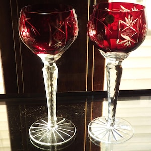 Pode incluir: Duas taças de vinho de vidro transparente com vinho tinto dentro. As taças têm um design de vidro cortado e estão sobre uma superfície preta.