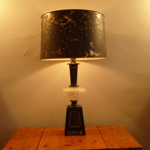May include: A black and gold table lamp with a white frosted glass shade. The lamp has a decorative base with a geometric design.