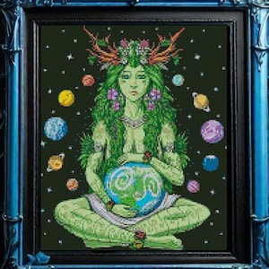 May include: A framed cross-stitch artwork featuring a green figure holding a globe, surrounded by planets against a dark green background. The figure wears a floral crown and is framed in a blue ornate frame. The artwork evokes themes of nature and spirituality.
