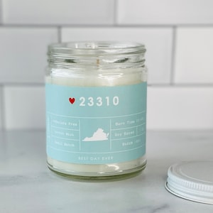 May include: A light blue candle jar with a white lid. The jar has a white label with the text "23310" and a red heart. The label also includes the text "BEST DAY EVER" and details about the candle, such as "Inthalate Free", "Cotton Wick", "Small Batch", "Burn Time 50 hrs", "Soy Based", and "Batch 1461".
