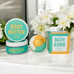 May include: A set of bath and body products in a gardenia and tuberose scent. The set includes a body butter, a sugar scrub, and a bath bomb. The products are all in white jars and boxes with green and gold accents.