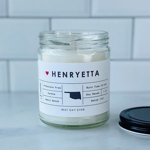 Puede incluir: Una vela blanca en un tarro de vidrio con una etiqueta en blanco y negro que dice "HENRYETTA" y "BEST DAY EVER". La etiqueta también incluye detalles sobre la vela, como "Phthalate Free Candle", "Small Batch", "Burn Time 50 HRS", "Soy Based 7 OZ", y "Batch 1907".