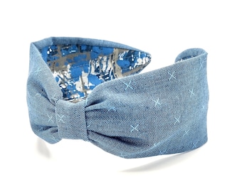 May include: A blue denim headband with a bow and a subtle pattern of small white crosses. The headband is reversible, with a blue and white floral pattern on the other side.