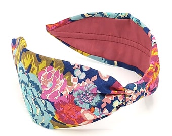 May include: A blue and floral patterned headband with a knotted design. The headband is made of fabric and has a pink lining.