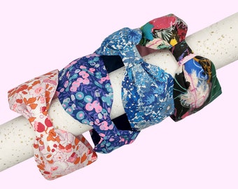 May include: Four colorful fabric headbands with knotted bows. The headbands are in shades of blue, pink, orange, and green with floral patterns.