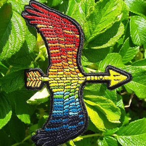 Op de afbeelding: Regenboogkleurige geborduurde strijkpatch van een vliegende vogel met een pijl in zijn bek.