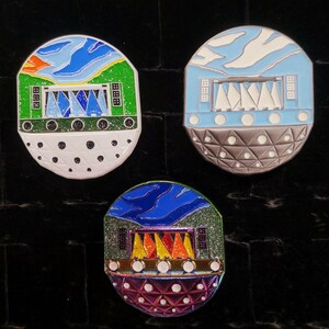 May include: Three enamel pins featuring a stylized illustration of a domed building with a stage and lights. The pins are in different color schemes: green, blue, and purple.