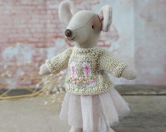 May include: A small, gray, plush mouse wearing a beige knitted sweater with pink bunny ears embroidered on the front and a pink tulle skirt.
