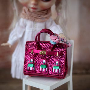 Può includere: Una borsa a mano rosa scintillante con dettagli dorati e un design a fantasia rosa e bianca. La borsa ha un manico superiore e una chiusura a scatto.