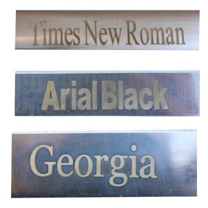 Może przedstawiać: Trzy metalowe płytki z wygrawerowanymi na nich r&oacute;żnymi czcionkami. G&oacute;rna płytka zawiera napis "Times New Roman", środkowa płytka zawiera napis "Arial Black", a dolna płytka zawiera napis "Georgia".