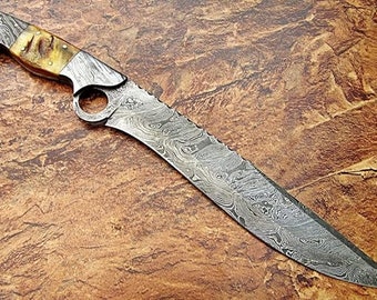 May include: A large, silver, Damascus steel knife with a brown and white handle. The blade has a serrated edge and a hole in the blade near the handle.