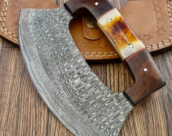 May include: A curved, stainless steel cleaver with a wood and bone handle. The blade has a wavy, damascus pattern. The cleaver is shown with a leather sheath.