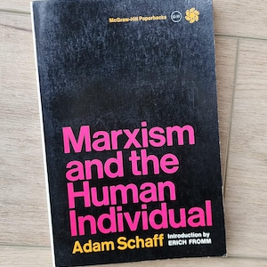 Puede incluir: Un libro de bolsillo titulado "Marxismo y el Individuo Humano" de Adam Schaff. La portada negra presenta el título en rosa y el logotipo de McGraw-Hill Paperbacks. La introducción es de Erich Fromm.