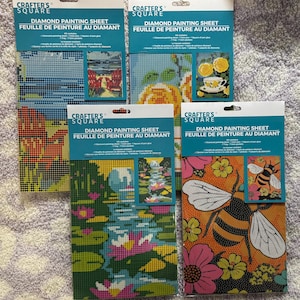 May include: Four diamond painting kits from Crafter's Square. Each kit features a different design, including a beach scene, roses with a teacup, a pond with lily pads, and a bee with flowers. The packaging includes the text "Diamond Painting Sheet" and "Feuille de peinture au diamant."