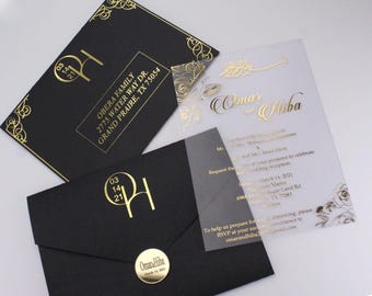 Pode incluir: Um convite de casamento preto e dourado com uma sobreposição de acrílico transparente. A sobreposição apresenta os nomes do casal, "Omar & Hiba", em escrita dourada. O convite inclui a data, a hora e o local da recepção de casamento. O convite é decorado com desenhos florais dourados.