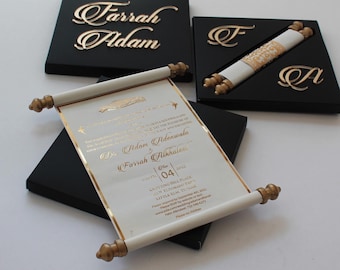 Pode incluir: Um rolo branco com detalhes dourados, contendo um convite de casamento para Adam Adenwale e Farrah Alkhalee. O rolo está enrolado e amarrado com uma fita dourada. O convite está em uma caixa preta com os nomes do casal na parte superior.