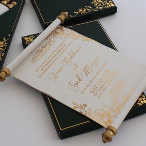 Puede incluir: Rollo blanco con letras doradas y diseños florales. El rollo está enrollado y atado con una cinta dorada. El texto en el rollo dice: "MR. AND MRS. YARTA KARBAN THE HONOR OF YOUR PRESENCE AT THE WEDDING RECEPTION OF THEIR DAUGHTER Anam Rabban Soud Mary SON OF MR. AND MRS. NIRMAT SAT 25 JUN TWO THOUSAND TWENTY-THREE AT SIX THIRTY PM"