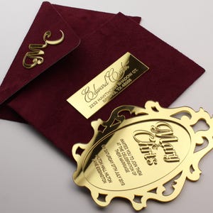 以下が含まれることがあります： 金色のアクセントが付いた、バーガンディ色の招待状セット。 金色のモノグラム、長方形の名札、装飾的な招待状カードが含まれています。 招待状カードには「Mary & Chris」と書かれており、結婚式の日付と場所が記載されています。