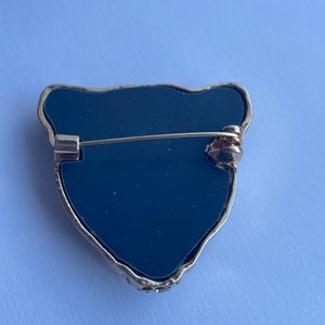 May include: Black onyx brooch with a gold-tone setting in the shape of a bear's head. The brooch has a pin and catch closure on the back.