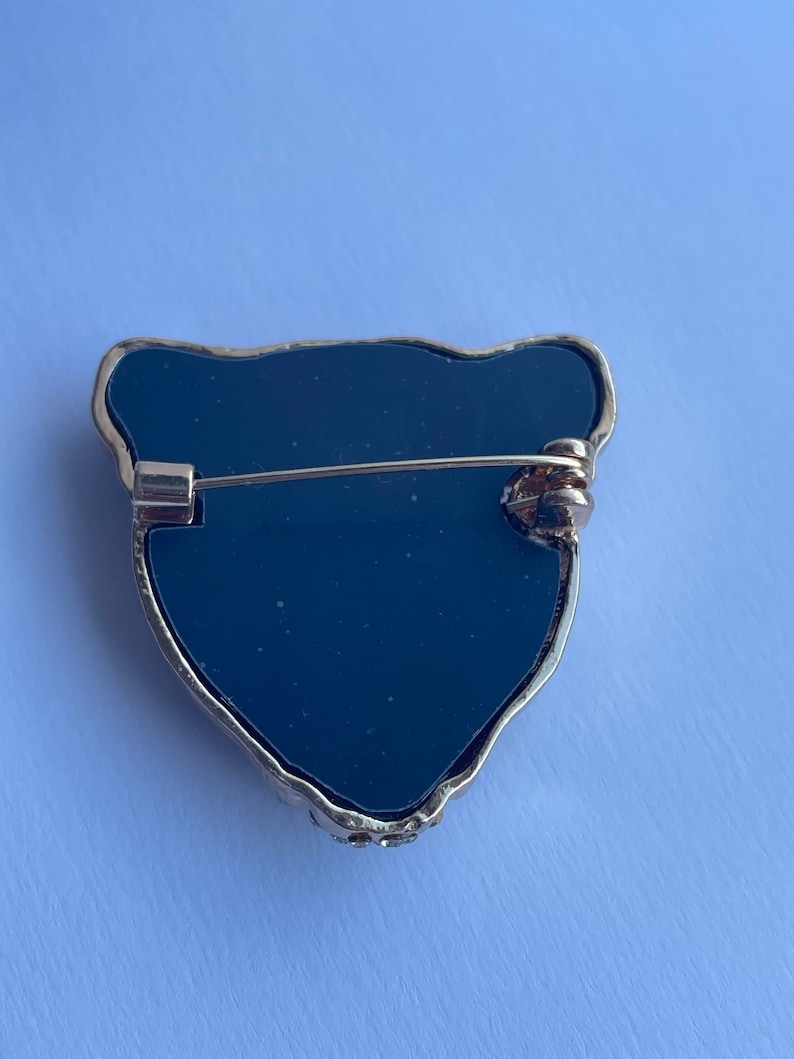 May include: Black onyx brooch with a gold-tone setting in the shape of a bear's head. The brooch has a pin and catch closure on the back.