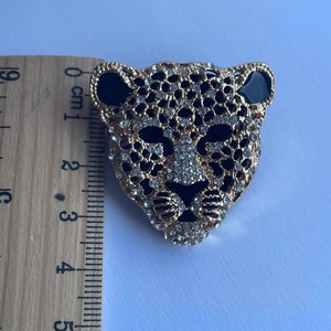 May include: Gold-tone brooch with a black and white leopard design. The leopard's face is covered in rhinestones.
