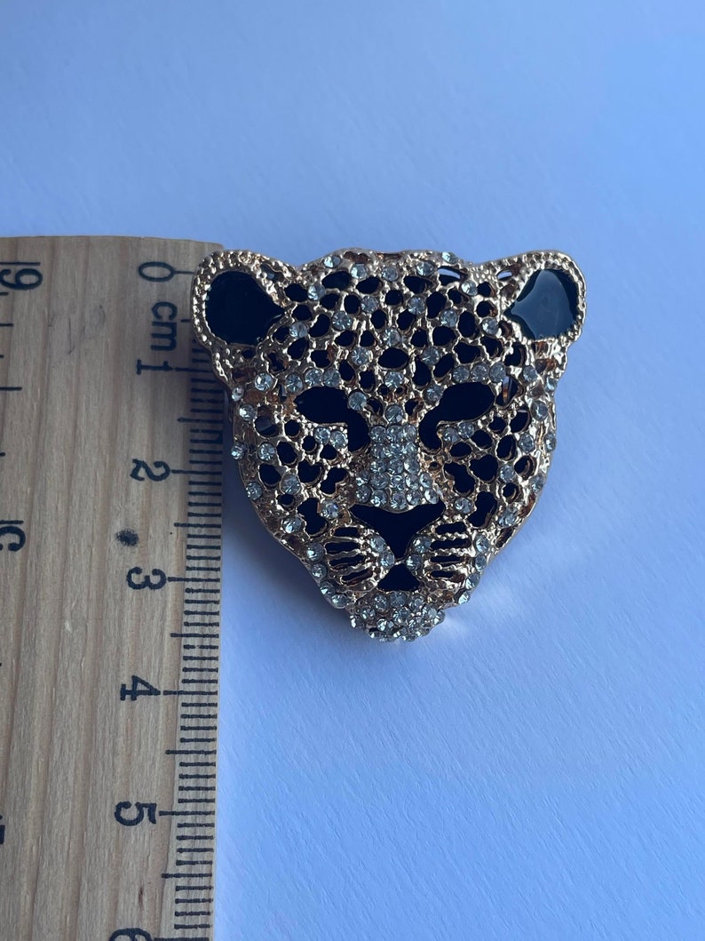 May include: Gold-tone brooch with a black and white leopard design. The leopard's face is covered in rhinestones.