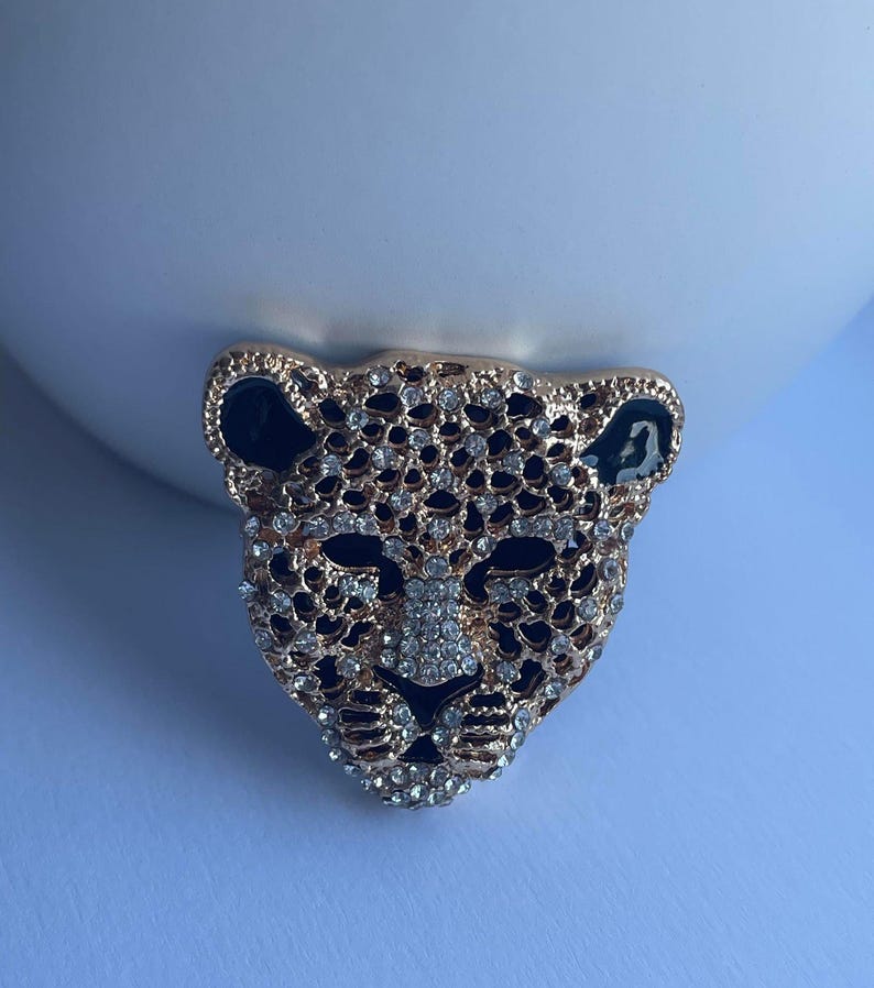 May include: Gold-tone brooch with a black and white leopard design. The leopard's face is covered in rhinestones.