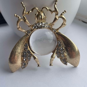 Op de afbeelding: Een gouden bij broche met heldere strass steentjes en een rond, helder glazen centrum.