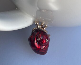 May include: A red anatomical heart charm with gold detailing. The heart is three-dimensional and has a realistic appearance.